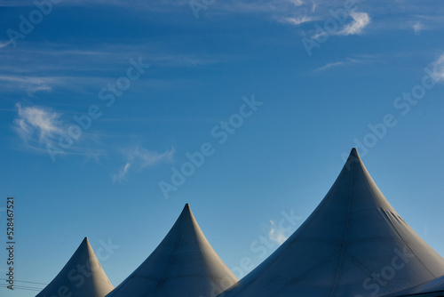 Tent roofs against the blue sky and clouds. A row of white triangular pyramid marquee rooftops against a blue sky