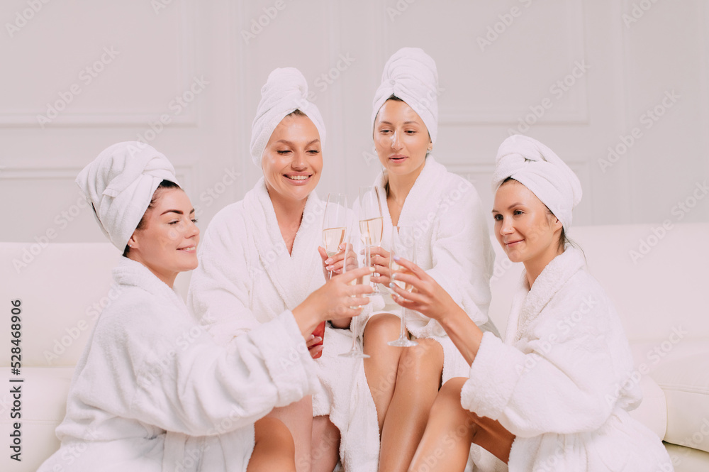 A group of women spend leisure time. Young attractive females in bathrobes drink champagne and chat merrily. A group of women spend leisure time. Young attractive females in bathrobes drink champagne and chat merrily.