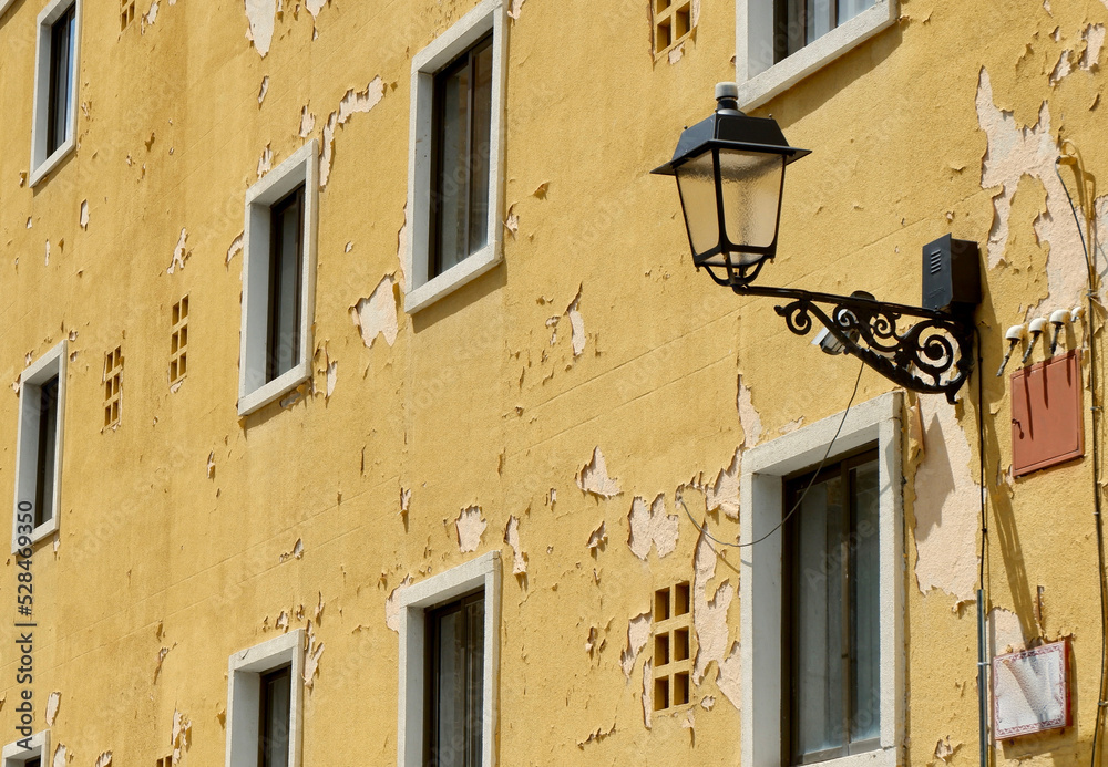 Damaged facade with simple windows and yellow peeling paint in Segovia, Spain