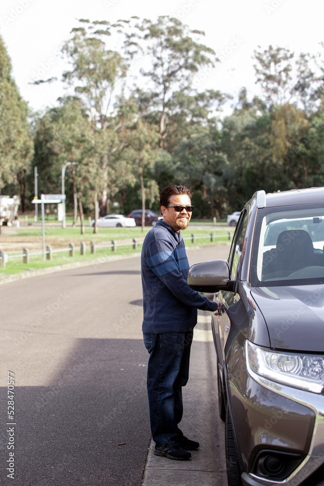 smiling middle aged man wearing blue sweater and sunglasses holding the car door handle smiling middle aged man wearing blue sweater and sunglasses holding the car door handle