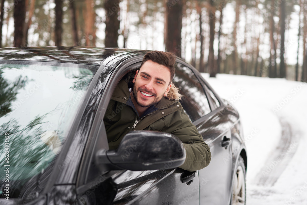 Young attractive Caucasian man sits at the wheel of his car sunny winter day.