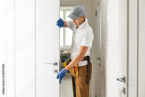 A craftsman with an electric screwdriver in his hands inserts a lock into the door. Tighten the screw in the door lock