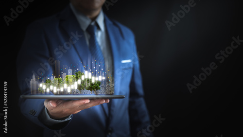 Businessman holding a tablet with graphs and virtual cities, urban economic management concept, reliable leadership.