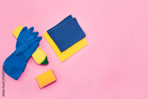 household supplies for cleaning the apartment, a blue rag, gloves and a yellow sponge on a pink background