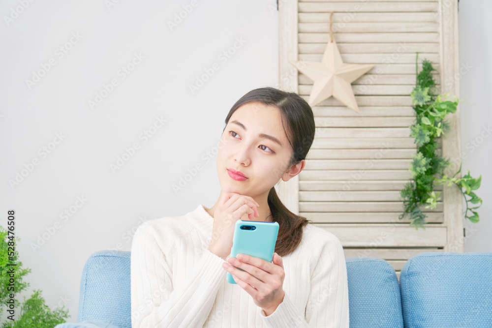 リビングでスマホを持って考える女性