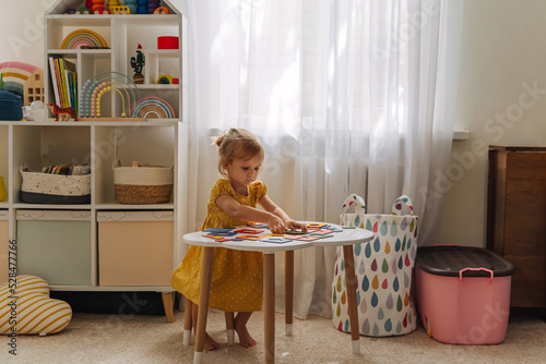 A little girl playing with wooden shape sorter toy on the table in playroom. Educational boards for Color and Shapes sorting for toddler. Learning through play. Developing Montessori activities. photo