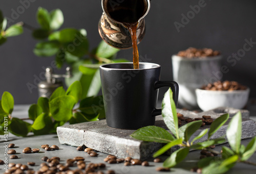 Coffee is poured into a black mug from a metal cup on a dark background. photo
