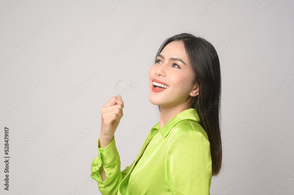 Young smiling woman holding invisalign braces in studio, dental healthcare and Orthodontic concept.