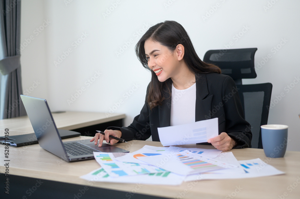 Young beautiful business woman working on laptop with documents in modern office Young beautiful business woman working on laptop with documents in modern office