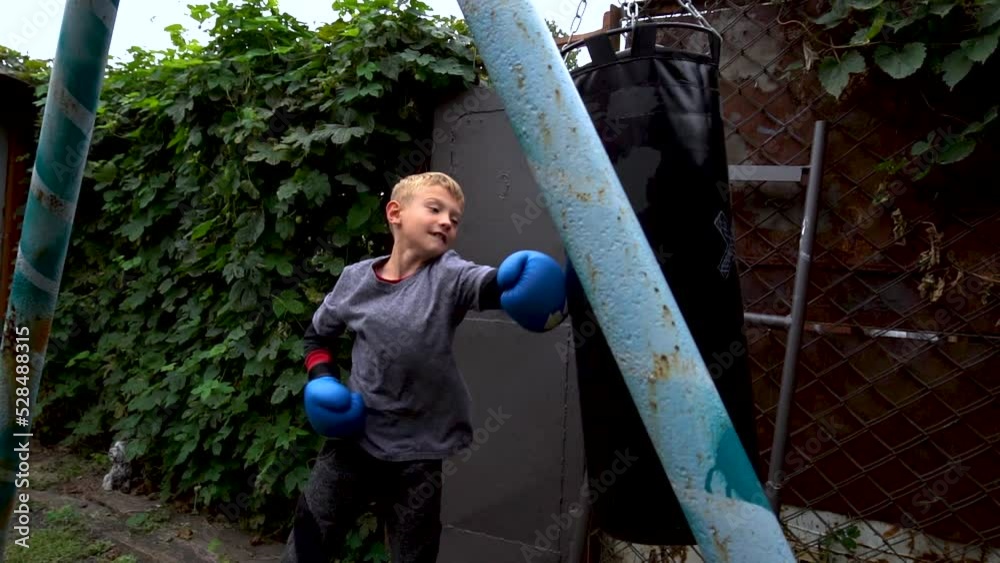 a boy punches a punching bag in blue gloves in the yard a boy punches a punching bag in blue gloves in the yard