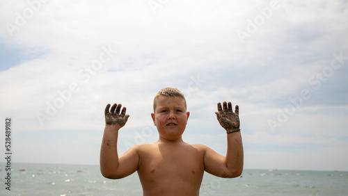 a boy on a sandy beach. the boy raised his hands and shows how the sand stuck to his hands