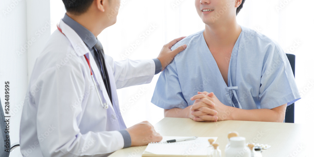 Unrecognizable Male doctor and young male patient while consult and .explain. Doctor and patient sitting together at table in clinic Unrecognizable Male doctor and young male patient while consult and .explain. Doctor and patient sitting together at table in clinic