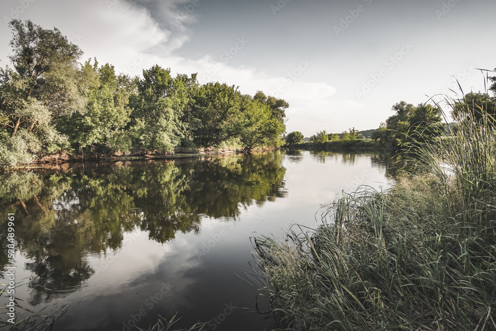 The mirror water surface of the steppe river Slobozhanshchina in the summer months reflecting green trees and the sky The mirror water surface of the steppe river Slobozhanshchina in the summer months reflecting green trees and the sky