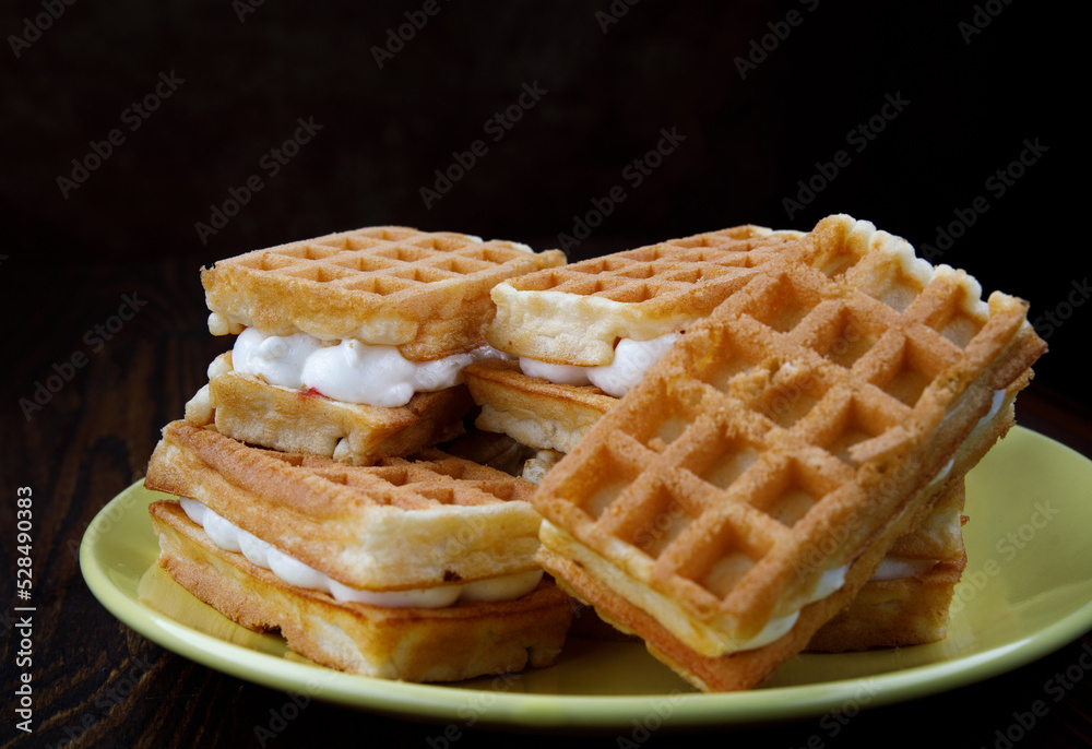 A pile of fresh Viennese waffles lie on a yellow plate.