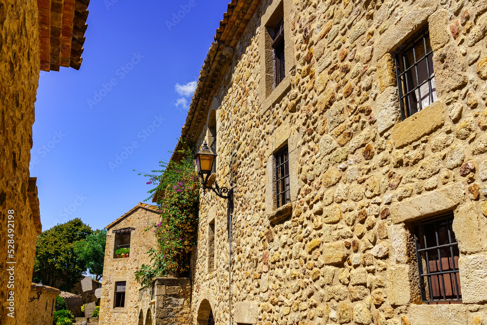 Facades of old houses made of stone with barred windows and wooden doors, Pals, Girona.