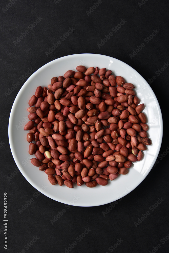 Peanuts on a white plate on a black background. Delicious nutty breakfast. Peanuts on a white plate on a black background. Delicious nutty breakfast.