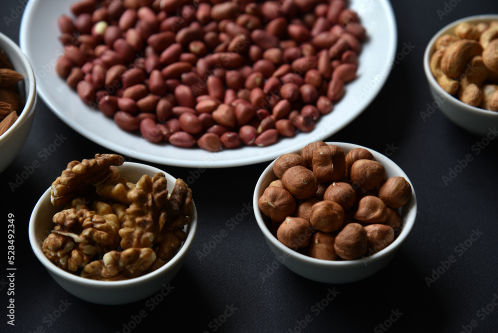 Peanuts on a white plate on a black background. Delicious walnut breakfast with walnuts, cashews and almonds. Peanuts on a white plate on a black background. Delicious walnut breakfast with walnuts, cashews and almonds.