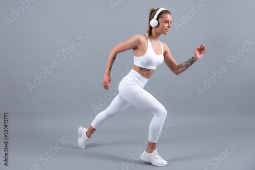 Fitness woman runner. Sporty strong cheerful young woman posing on gray isolated background. Caucasian female athlete, muscular, sportive woman. Concept of youth healthy lifestyle.