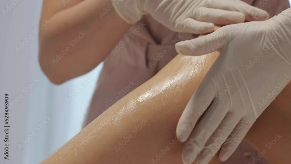 A female depilatory expert applies sugar paste on the patient's leg. The process of hair depilation on the girl's leg with sugar paste by a professional master. A female depilatory expert applies sugar paste on the patient's leg. The process of hair depilation on the girl's leg with sugar paste by a professional master.