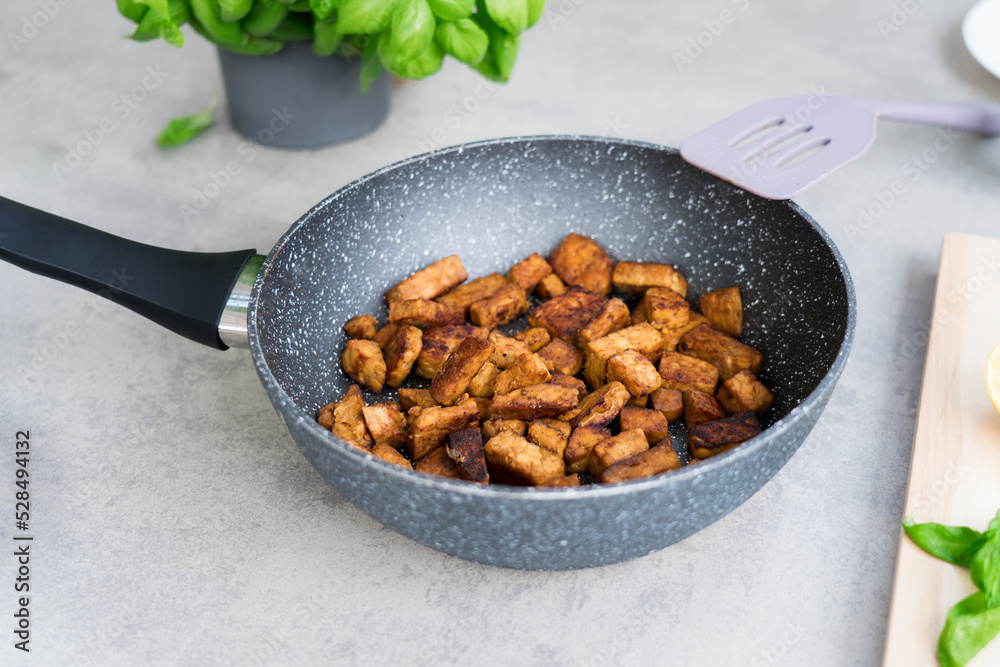 Fototapeta premium Roasted Tempeh or Tempeh, made of fermented soybean seeds. Fried cubed Tempeh in the pan. Soya protein. Plant based meat. Healthy Cooking and eating. Go vegan. Selective focus, copy space