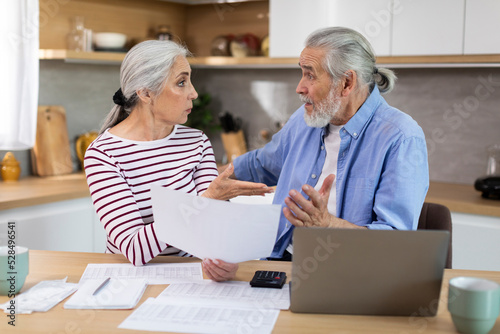 Worried Elderly Spouses Checking Financial Documents In Kitchen At Home