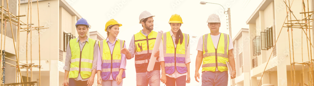 Group of happy contractors, engineers and formats in safety vests with helmets stand on the under-construction building site. teamwork concept. Group of happy contractors, engineers and formats in safety vests with helmets stand on the under-construction building site. teamwork concept.
