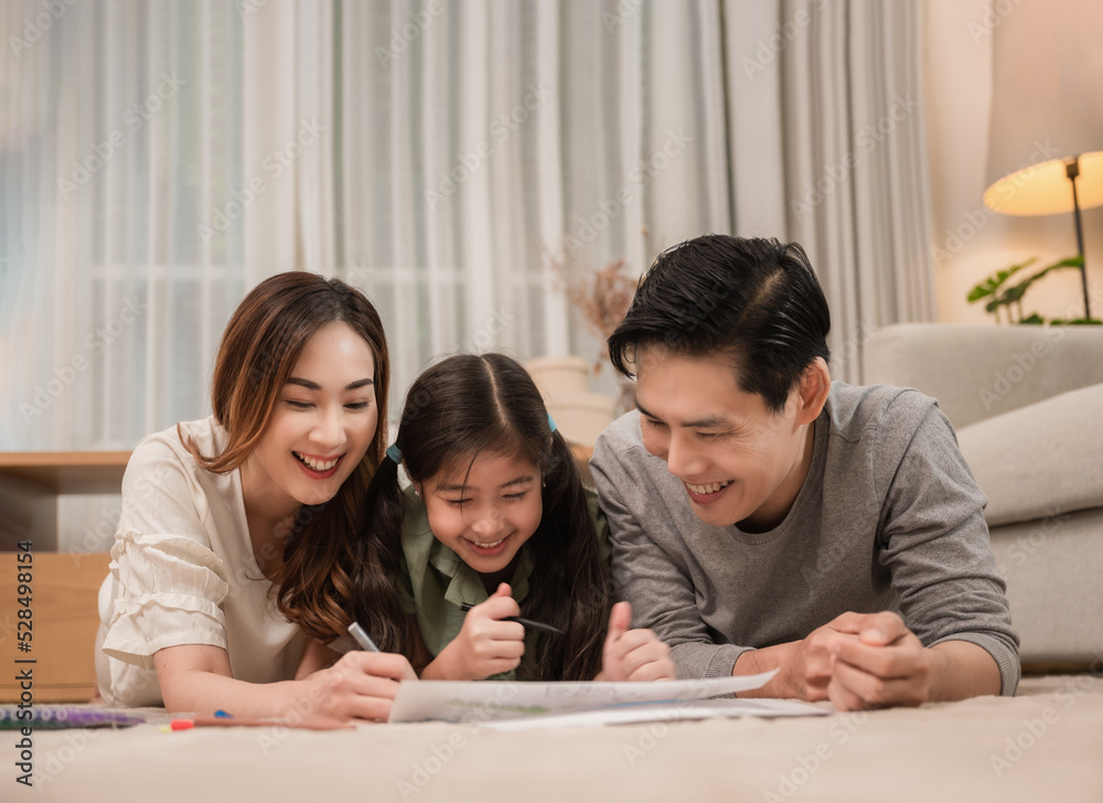 Happy Asian family father, mother, and daughter relaxing by playing and painting together on carpet in the living room at home. Happy Asian family father, mother, and daughter relaxing by playing and painting together on carpet in the living room at home.