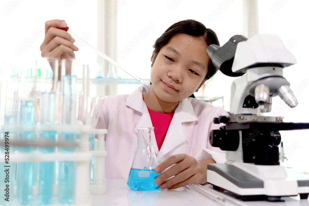 Adorable schoolgirl in lab coat doing science experiments, young scientist adding some chemical to blue flask with pipette and learning science experiment in laboratory. Asian kid using microscope, ap Adorable schoolgirl in lab coat doing science experiments, young scientist adding some chemical to blue flask with pipette and learning science experiment in laboratory. Asian kid using microscope, ap