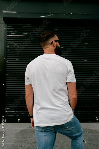 Young bearded hipster guy wearing white blank t-shirt and blue jeans in a random urban style. Design men t shirt mock-up for print