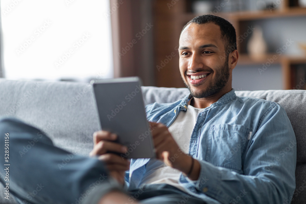 Handsome smiling black male relaxing with digital tablet at home