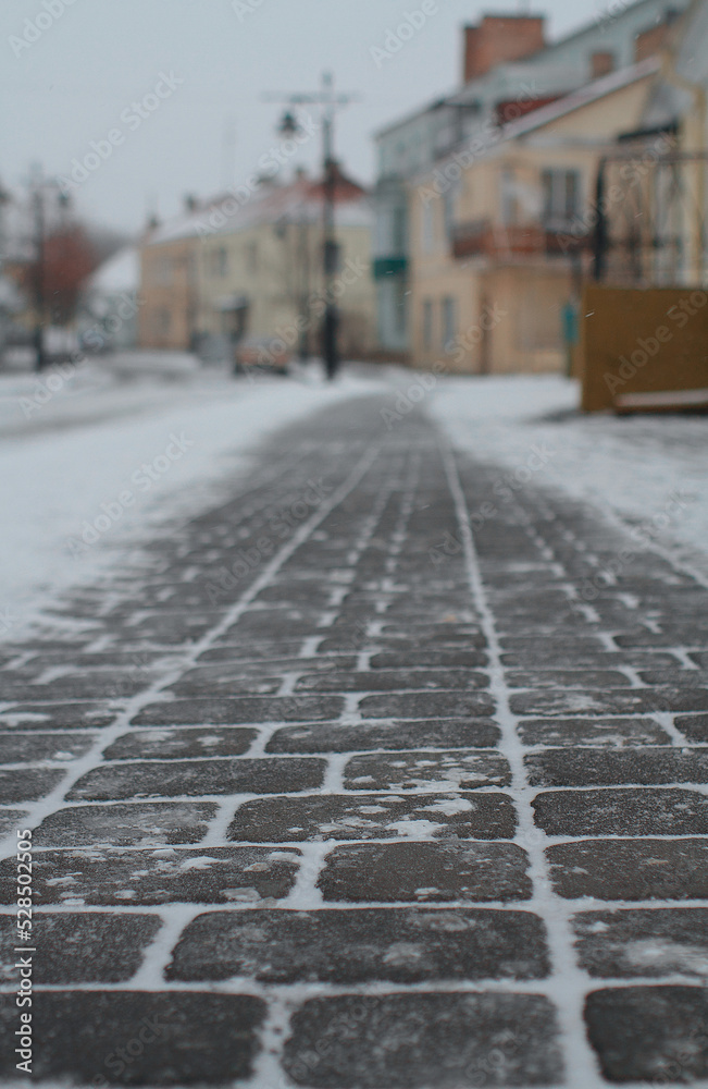 Old pavement in town Lutsk. Shallow depth of field, selective focus. Winter view of Cathedral Street in the Old Town of Lutsk. Fresh snow is falling, Christmas time