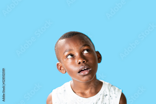 Ritratto di ragazzo africano carino che guarda in alto, pensa a qualcosa con la Boca aperta, trovando una buona idea photo