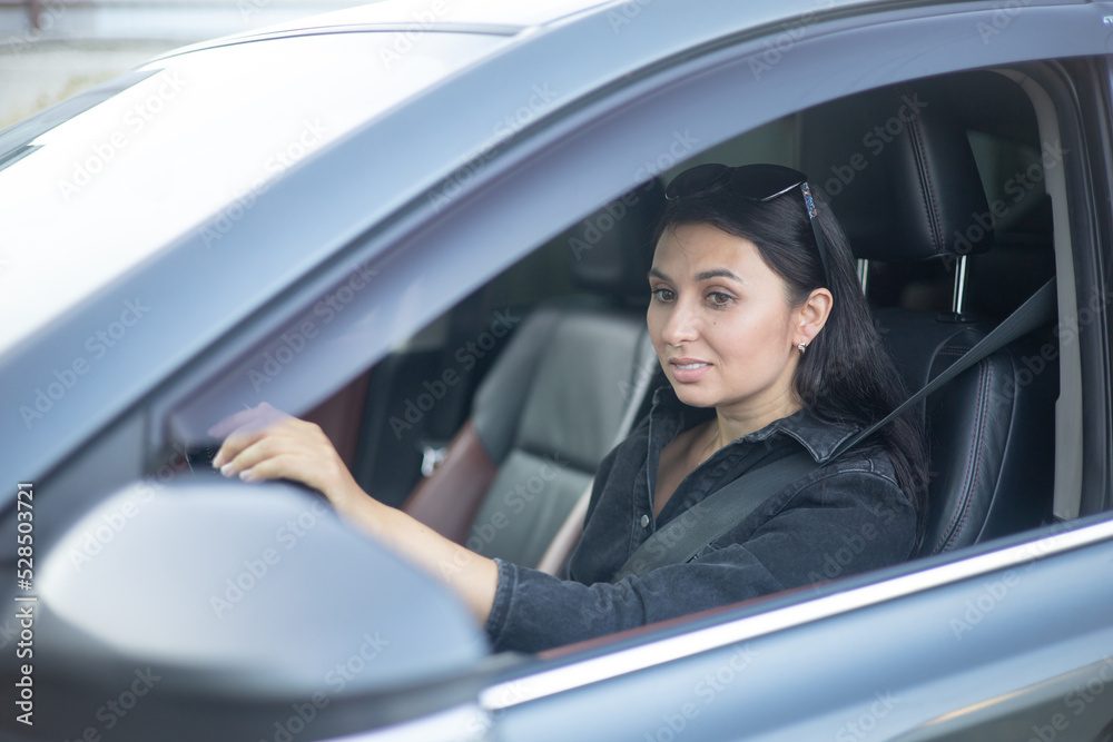 A young beautiful woman is the driver in her car in town. Commute, commute. Lifestyle