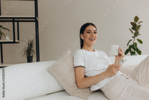 A woman is drinking coffee and using on a cell phone at home