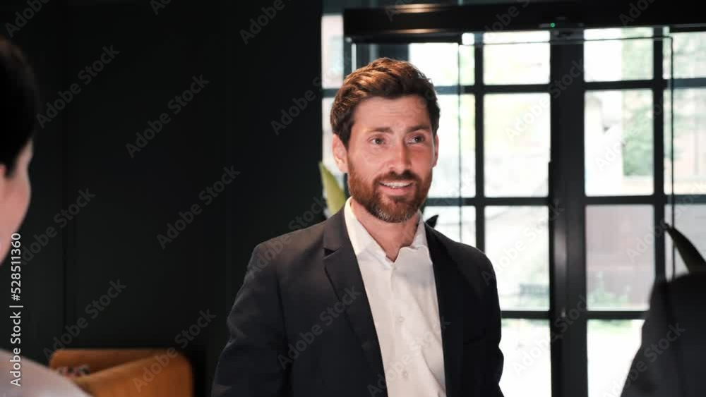 Elegant fashionable businessman with suitcase enters arriving in hotel to reception greets the staff receives a key card from the room during business trip. Posh hotel for check-in settling.