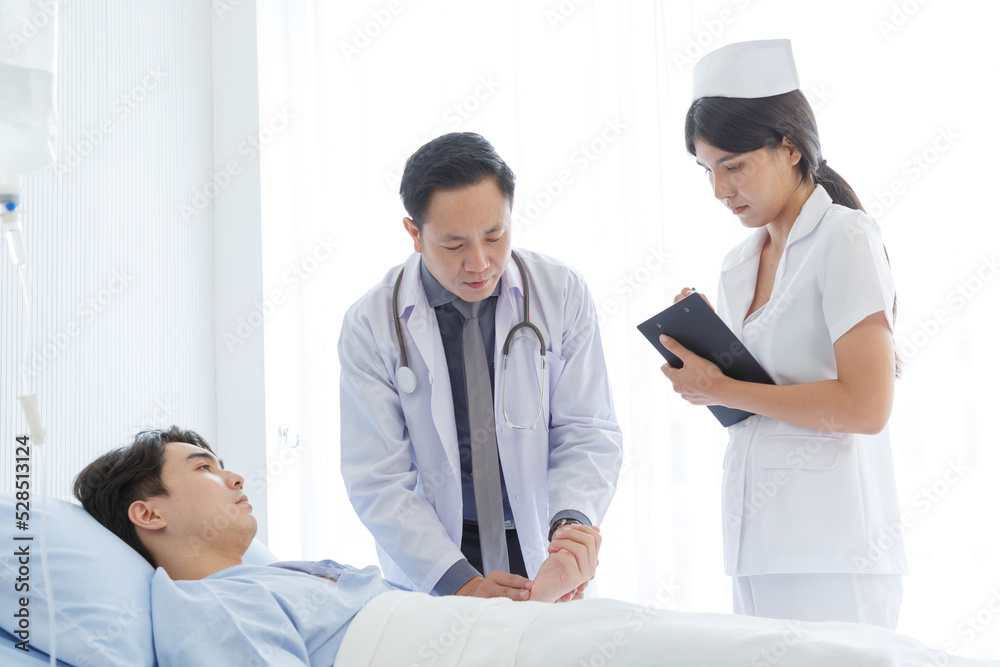 Senior doctor and young male patient who lie on the bed while checking symptom, consult and explain with nurse taking note and supporting in hospital wards.