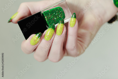 Woman's hand with long nails and bright yellow green thermo manicure with bottles of nail polish photo