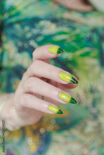 Woman's hand with long nails and bright yellow green thermo manicure with bottles of nail polish photo