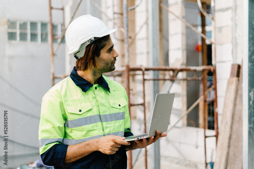 On building construction site, Construction engineers with safety hardhat and in vest use a laptop computer On building construction site, Construction engineers with safety hardhat and in vest use a laptop computer