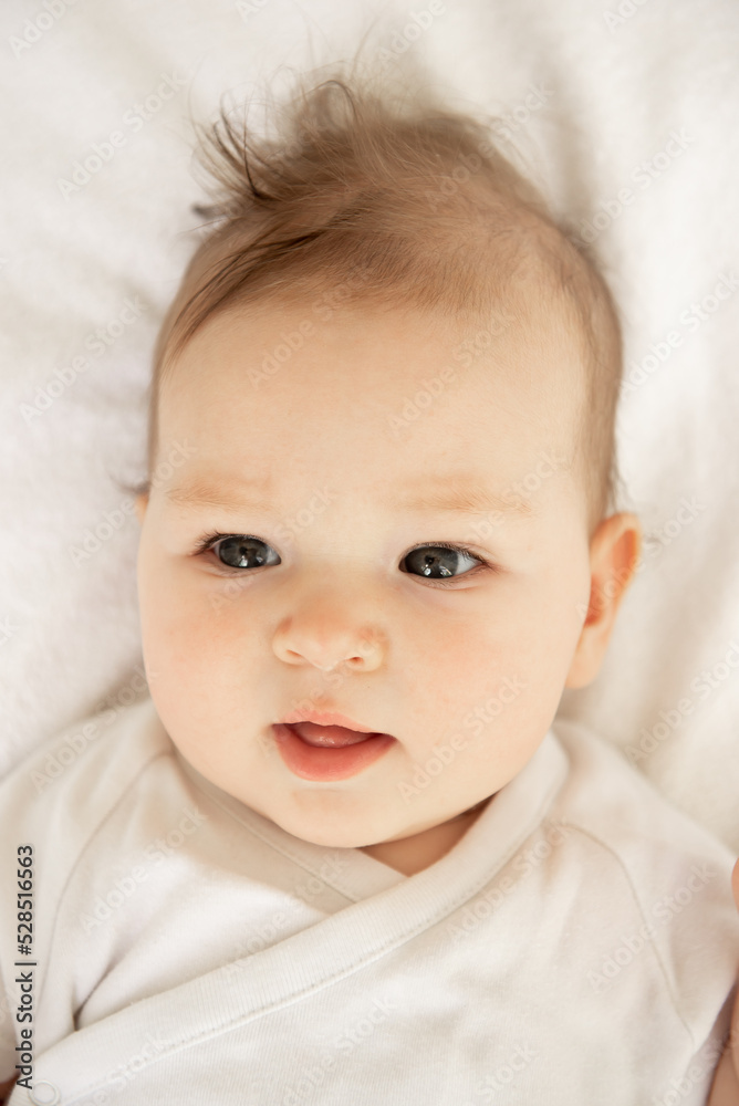 Portrait of a very beautiful little baby girl with blue eyes lies on the bed.
