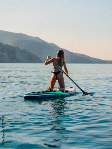 Sporty girl rowing on stand up paddle board at sea. Woman on SUP board in sea © artifirsov