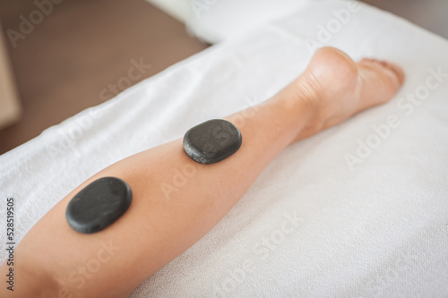 Energy black stones. Woman getting hot spa volcanic lava stone therapy, legs massage procedure in salon. Body care healthy lifestyle. Beauty treatment. Maderotherapy.