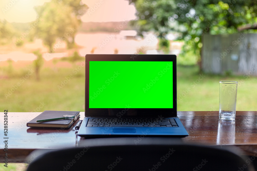 Fototapeta premium Green screen notebook with notebooks placed on a wooden table against a beautiful natural scenery background.