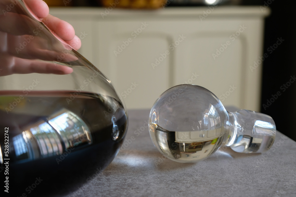 Decorative glass cork and carafe of red wine in the kitchen interior. Hand on the decanter. Selective focus. Decorative glass cork and carafe of red wine in the kitchen interior. Hand on the decanter. Selective focus.