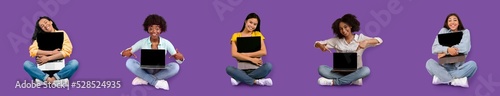 Smiling young international females sitting, hugging laptop with blank screen, isolated on purple background © Prostock-studio
