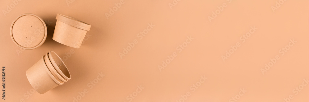 Banner with brown paper food containers for soup or ice cream, cup with paper cap over light brown background with copy space, mockup image. Sustainable food packaging. Monochrome Banner with brown paper food containers for soup or ice cream, cup with paper cap over light brown background with copy space, mockup image. Sustainable food packaging. Monochrome