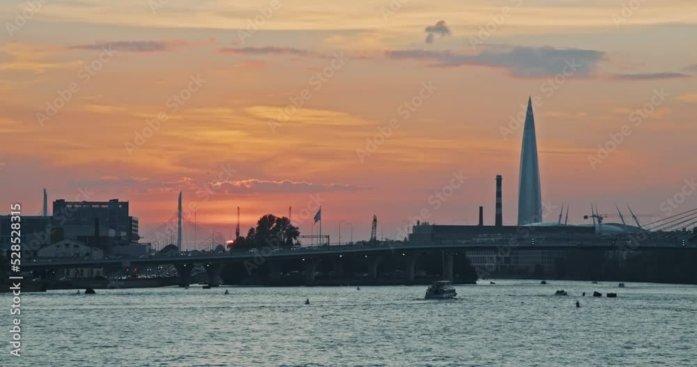 Sunset in Saint Petersburg. The sun is almost over the horizon. Peach sky. Lots of cars going fast across the bridge. Pleasure and sightseeing boats are floating on the water. Busy city. View of the Sunset in Saint Petersburg. The sun is almost over the horizon. Peach sky. Lots of cars going fast across the bridge. Pleasure and sightseeing boats are floating on the water. Busy city. View of the