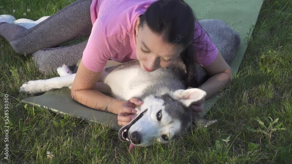 Young woman relaxing with her beautiful husky dog in the village meadow on the grass, kissing and hugging cute pet, adorable friendship between people and animals. Young woman relaxing with her beautiful husky dog in the village meadow on the grass, kissing and hugging cute pet, adorable friendship between people and animals.