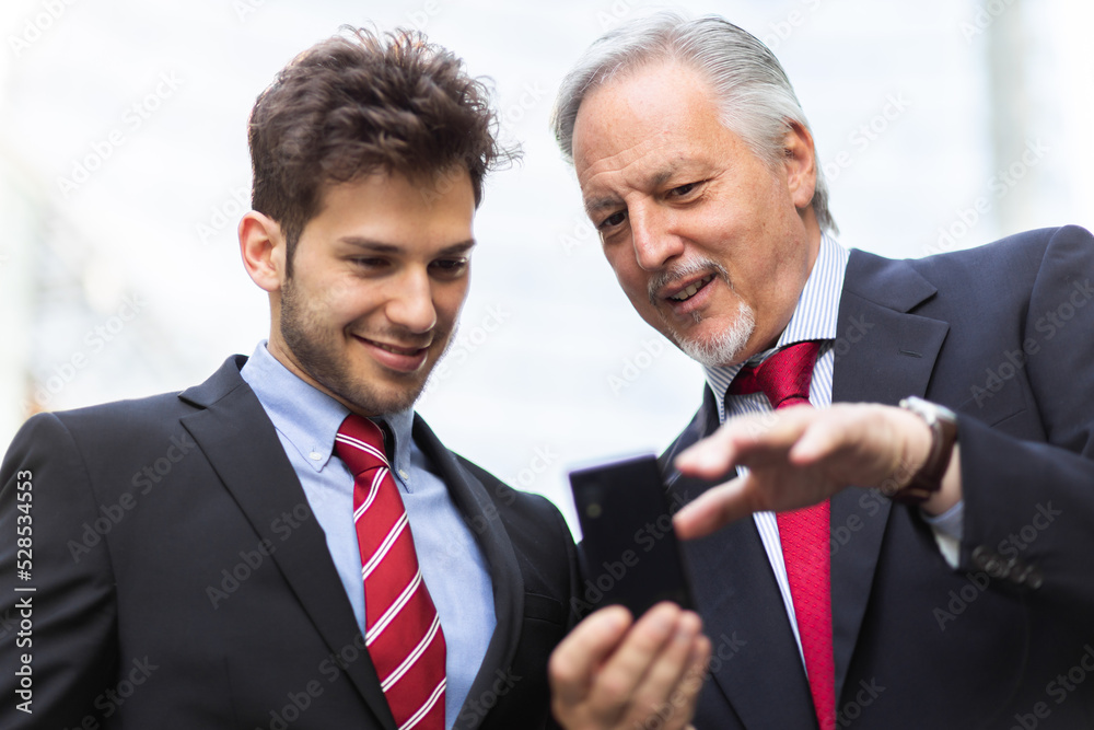 Senior manager showing something on a smartphone to his younger colleague Senior manager showing something on a smartphone to his younger colleague