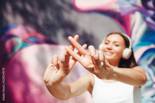 the girl makes a hashtag with her hands. a young woman wearing headphones shows a hashtag against the background of the street and graffiti